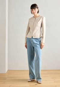 Beige läderjacka med en figurnära design, dragkedjestängning och sömdetaljer, kombinerad med ljusblå vida jeans och metalliska ballerinas.