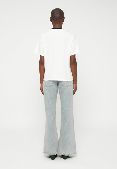 Vit kortärmad t-shirt med svart krage, i kombination med ljusblå utsvängda jeans. Slät tygtextur, minimalistisk design.