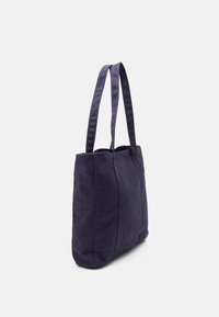 Sac en toile bleu marine avec deux longues poignées, de forme rectangulaire, surface texturée et coutures verticales sur le côté pour un détail supplémentaire.