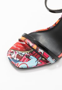 I sandali con tacco alto multicolori presentano una parte superiore in tessuto a fantasia nei toni di rosso, blu e nero, con eleganti cinturini alla caviglia in vernice nera.