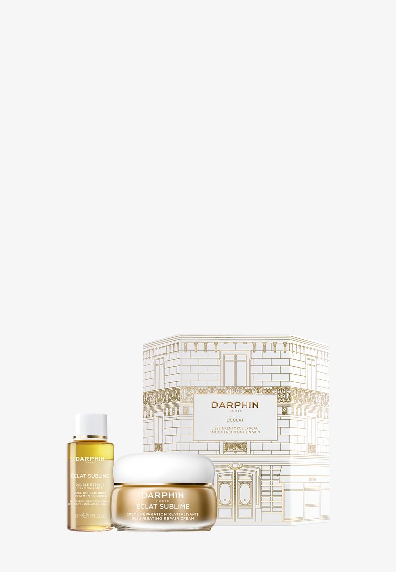 Le set Darphin Éclat Sublime comprend un pot en or de crème, une bouteille compte-gouttes dorée et une boîte décorée avec des éléments de design dorés et blancs.