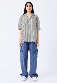 Gestreifte Button-Down-Bluse in Schwarz und Weiß, kombiniert mit weiten blauen Jeans-Cargohosen mit mehreren Taschen und ausgefranstem Saum.