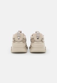 Beżowe sneakersy z panelami siateczkowymi, zaokrąglonym fasonem, wyściełanym kołnierzem i dwoma pętlami z tyłu. Posiadają srebrne akcenty na pięcie oraz grubą podeszwę.