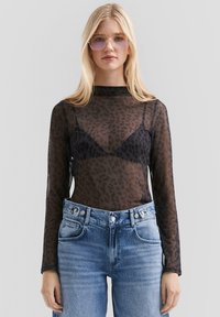 Schwarzes Mesh-Oberteil mit langen Ärmeln und Leopardenmuster, über einem schwarzen BH getragen, kombiniert mit hellen Denim-Jeans und goldfarbenen Sonnenbrillen.
