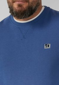 Felpa blu realizzata in tessuto misto cotone. Presenta un collo rotondo, cuciture testurizzate e un piccolo logo ricamato sul petto.