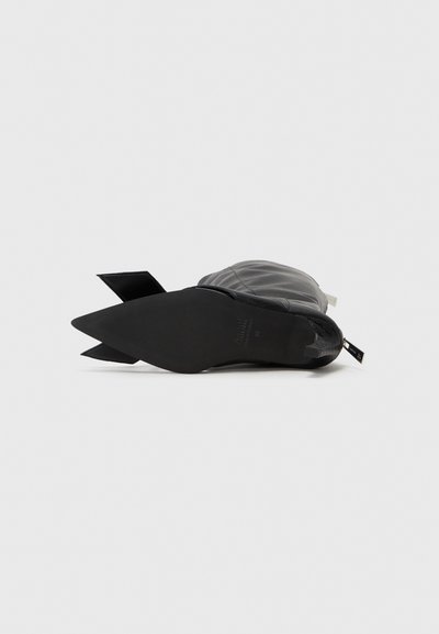 Botín de cuero negro hasta el tobillo con punta afilada, suela de goma plana y tirador decorativo en la parte trasera; presenta un acabado suave y un diseño minimalista.