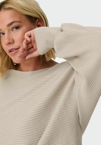Beige ribbed sweater with wide boat neckline and long, flowing sleeves. The texture is soft, featuring horizontal lines throughout.