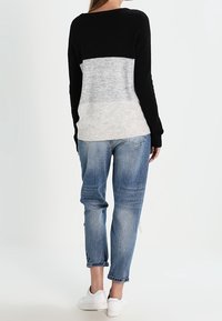 Sweter w czarno-szare bloki kolorystyczne o luźnym kroju, zestawiony z wyblakłymi niebieskimi zwężanymi dżinsami i białymi trampkami. Sweter o teksturowanym splocie z podwiniętymi mankietami.