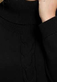 Svart turtleneck-tröja i strukturerad stickad tyg, med ett upphöjt kabelmönster nedanför mitten och ribbade manschetter.