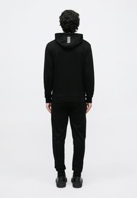 Conjunto deportivo negro compuesto por una sudadera con capucha y pantalones jogger. Presenta un diseño minimalista con un detalle de una franja blanca en la capucha.