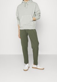 Ljusgrön hoodie med känguruficka och justerbara dragsnören, kombinerad med avslappnade olivgröna byxor och vita sneakers.