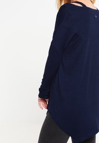 Haut manches longues bleu marine avec une coupe décontractée, doté d'un ourlet arrondi et d'un détail découpé sur les épaules. Texture du tissu douce.