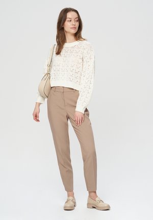 Maglione in maglia crema con un intricato design a lavorazione aperta, pantaloni beige su misura e mocassini chiari con suola spessa.