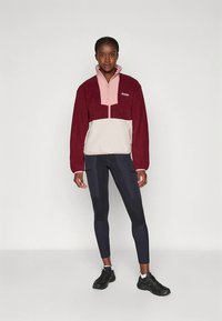 Bordó és rózsaszín polár pulóver negyed cipzárral és kontrasztos krémszínű betéttel. Fekete leggingssel és sportcipővel párosítva.