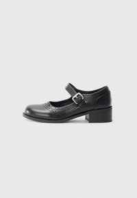 Black leather Mary Jane shoe with a round toe, ankle strap, and silver buckle. Features decorative perforations and a block heel.