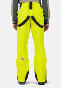 Pantaloni da sci gialli ad alta visibilità e impermeabili, con cintura rinforzata, bretelle regolabili e dettagli neri con zip sulle gambe.