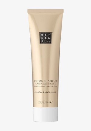 Goldfarbene Tube mit Detox-Shampoo-Konzentrat und weißem Deckel, beschriftet mit "Pink Clay & Apfelessig." Schwarzes Logo nahe der Oberseite, minimalistisches Design.