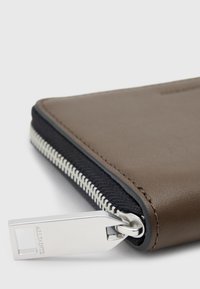 Portafoglio in pelle marrone con bordi in tessuto nero, dotato di chiusura a zip in argento e di un cursore della zip stampato con logo per un accesso facile.