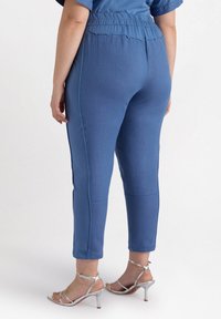 Blå ankel-långa byxor med elastisk midja, sidostrimmor och en slät yta. Kombineras med silverfärgade klackar med remmar.