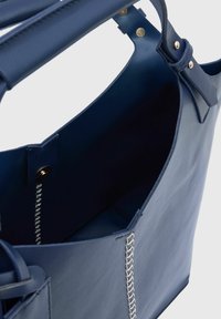 Leren tote bag in donkerblauw met een gladde textuur, open top en zichtbare binnenstiksels. Gouden hardware accentueert de handvaten.