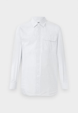 Bílá košile s dlouhým rukávem a knoflíkovým zapínáním, s jemnými vertikálními pruhy, náprsní kapsou s klopou na knoflík a klasickým límcem na jednobarevném pozadí.