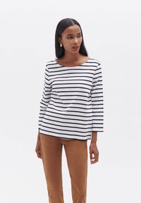 Weißes Langarmshirt mit marineblauen horizontalen Streifen, runder Ausschnitt und lässigem Schnitt, kombiniert mit braunen Hosen. Glatte Stoffoberfläche.