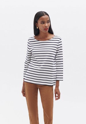 Camicia bianca a maniche lunghe con righe orizzontali navy, scollatura a barca e vestibilità comoda, abbinata a pantaloni marroni. Tessuto con texture liscia.