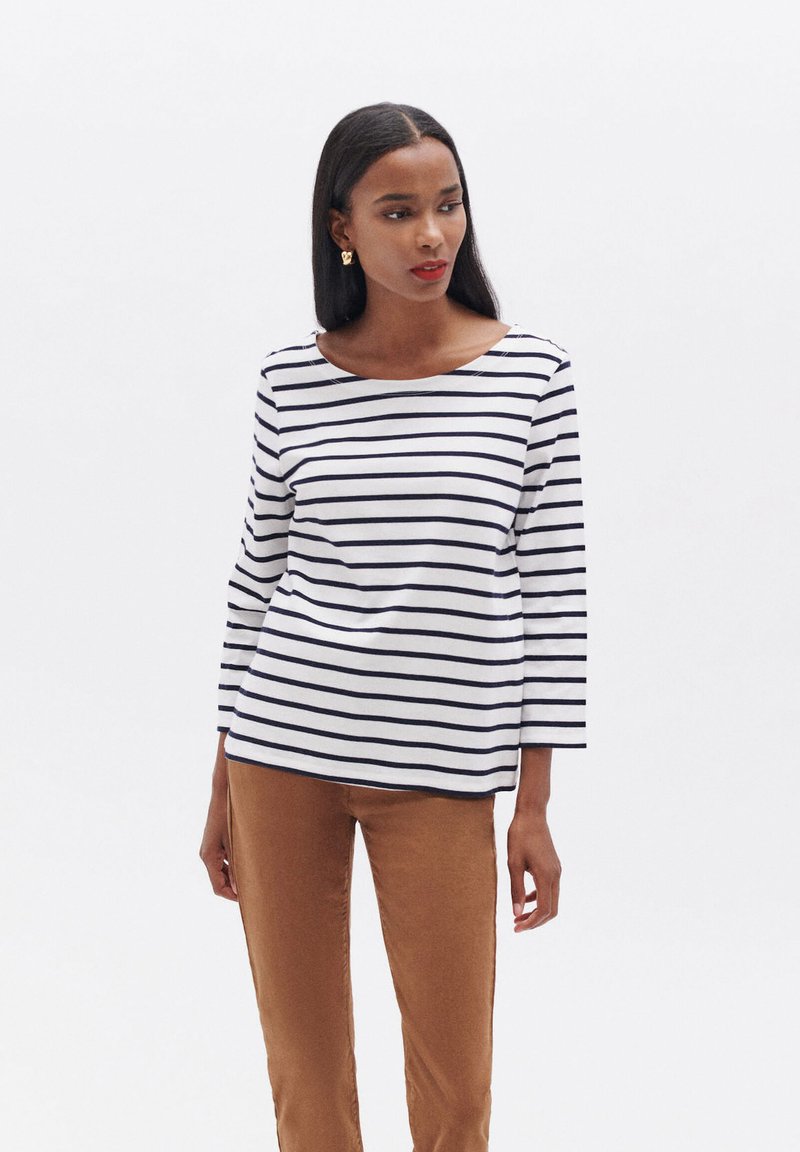Weißes Langarmshirt mit marineblauen horizontalen Streifen, runder Ausschnitt und lässigem Schnitt, kombiniert mit braunen Hosen. Glatte Stoffoberfläche.