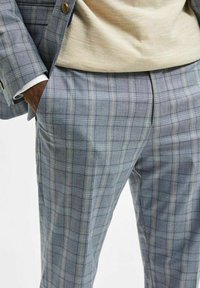 Ljusblå rutiga byxor gjorda av texturerat tyg, med subtila gula och marina linjer, fickor och en skräddarsydd passform.