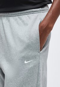 Ръка в джоба на светлосиви спортни панталони Nike, показваща бяло лого на Nike swoosh на лявото бедро.