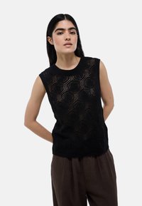 Haut sans manches noir avec un motif géométrique en tricot ouvert, encolure ras du cou et accents texturés, associé à un pantalon large marron.