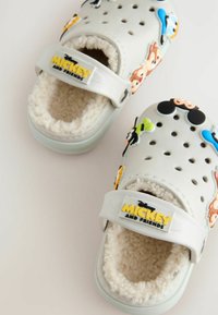 Sabots en caoutchouc blancs avec un intérieur en peluche, ornés de motifs colorés de personnages de dessins animés et d'une sangle jaune "Mickey et ses amis".