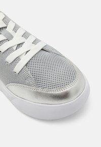 Silver mesh sneaker with white laces, round toe, and metallic accents. Features textured upper and a cushioned white sole.
