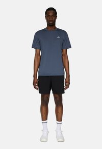 Grå kortärmad sporttröja med en liten vit logotyp, i kombination med svarta shorts och vita strumpor med svarta ränder. Vita sneakers.