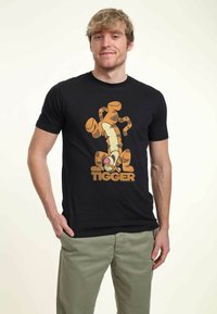 Svart bomulls t-shirt med en grafik av Tigger i orange och beige med texten "TIGGER" under. Designen har en lekfull, tecknad stil.