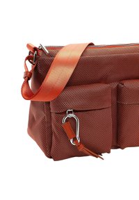 Borsa di tessuto rosso con texture, dotata di tracolla arancione regolabile, presenta due tasche frontali e un gancio in metallo argentato per fissare gli oggetti.