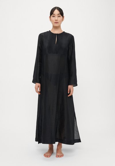 Robe noire à manches longues avec un haut plissé, un col rond, un détail d'ouverture en forme de trou de serrure à l'avant et des fentes latérales, fabriquée en tissu léger et transparent.