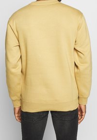 Yellow sweatshirt with a crew neckline, ribbed cuffs and hem, made from soft cotton fabric, worn with dark jeans.
