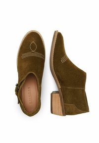 Botines de ante marrón con un bajo tacón de bloque de madera, costuras decorativas en blanco y cremallera lateral. Superficie texturizada y diseño de punta afilada.