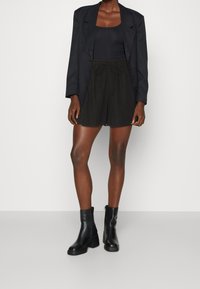 Pantaloni corti neri con cordoncino, realizzati in tessuto morbido, abbinati a un top aderente nero e a un blazer nero. Stivali neri alla caviglia completano l'outfit.