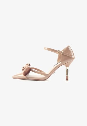 Chaussure à talon haut en cuir verni nude avec un bout pointu, une bride de cheville et un nœud décoratif en velours marron sur le devant.