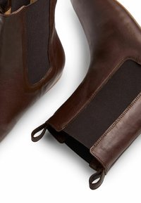 Botas de tobillo de cuero marrón con paneles laterales elásticos, puntera redonda y tiradores para facilitar su uso. Textura suave y diseño elegante.