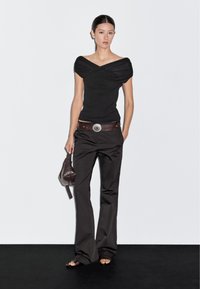 Sort off-shoulder top med draperinger, parret med slanke, mørke bukser og et brunt bælte med en sølvspænde. Brun håndtaske og sandaler.