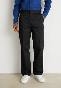 Schwarze Hose mit geradem Bein, aus gewebtem Stoff, mit flachem Bund und Taschen an der Seite, kombiniert mit weißen Sneakers.