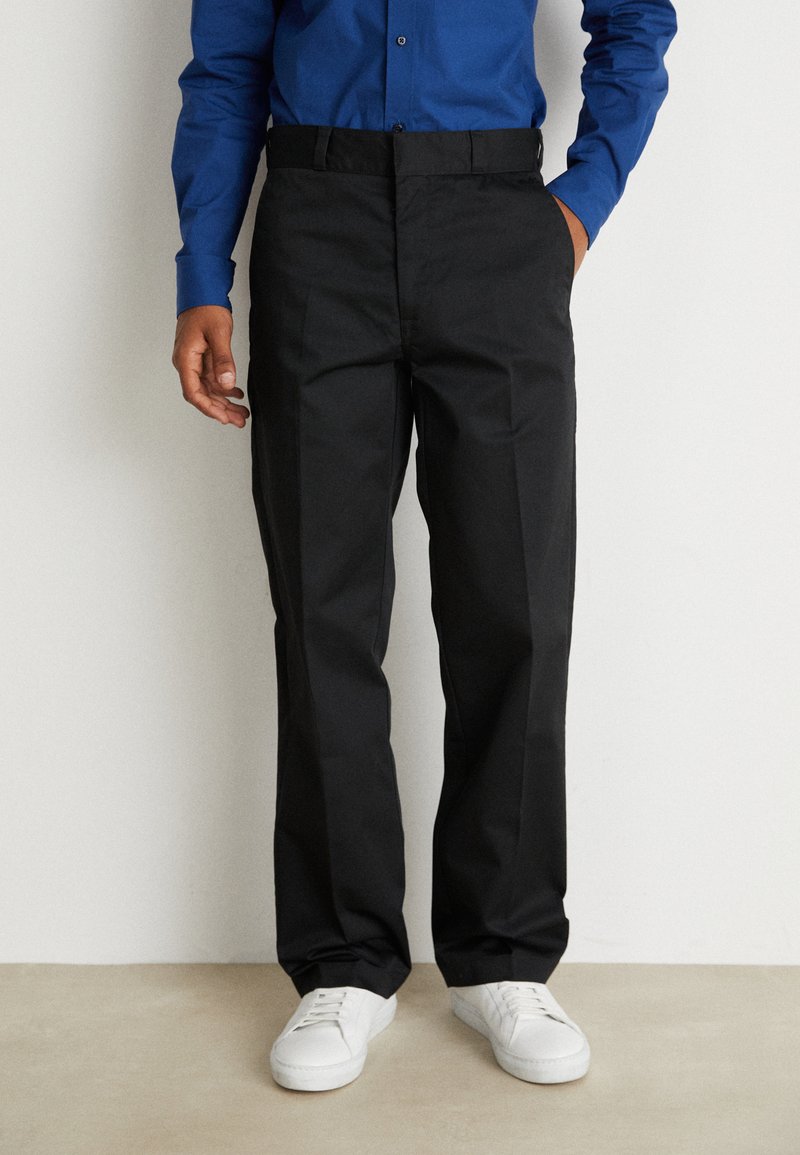 Schwarze Hose mit geradem Bein, aus gewebtem Stoff, mit flachem Bund und Taschen an der Seite, kombiniert mit weißen Sneakers.