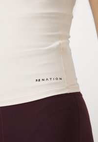 Kermakotim urheilu yläosa P.E Nation -logolla, joka on yhdistetty tumman burgundinvärisiin legginsseihin. Sujuva pinta, istuva muotoilu ja kontrastivärinä yhdistelmä.