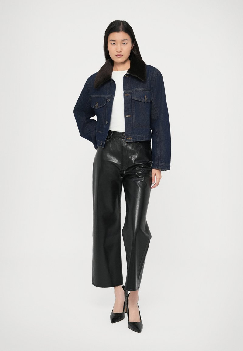 Giacca di denim con tessuto blu scuro e collo in pelliccia sintetica marrone, abbinata a pantaloni in pelle nera a vita alta e scarpe nere con tacco.