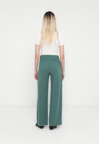 Videbukser i dempet grønn stoff, med elastisk midjebånd. Jevn tekstur, hel lengde, og minimalistisk design.