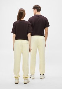 Μαύρα κοντοκομμένα μπλουζάκια και κίτρινες φόρμες με ελαστικά μανσέτες, φορεμένα από δύο μοντέλα, που παρουσιάζουν ένα απλό και καθημερινό σχέδιο.