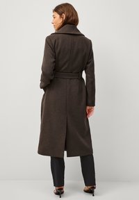 Lungo cappotto di lana marrone con cintura in vita, collo ampio e spacchetto centrale. Presenta una texture uniforme e una vestibilità sartoriale, adatta per abbigliamento formale.